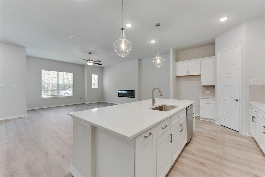 Kitchen featuring backsplash, ceiling fan, light hardwood / wood-style floors, sink, and a center island with sink