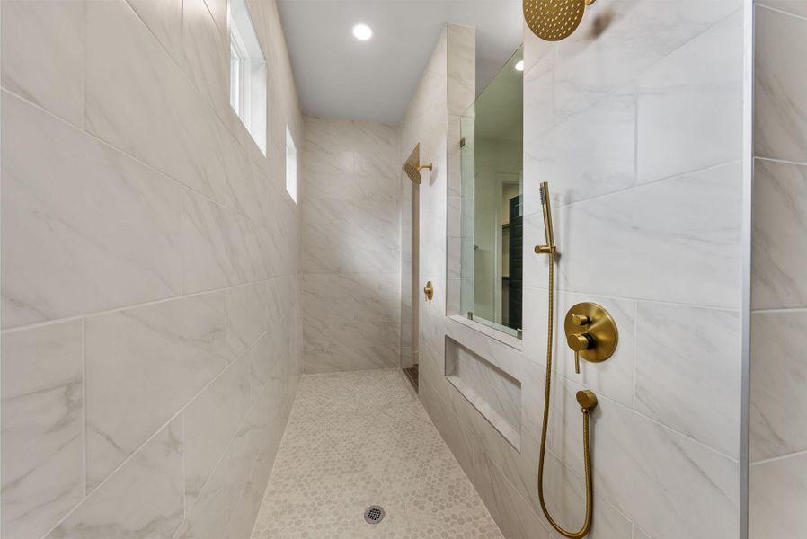 Marble-clad shower with gold fixtures and subtle window lighting offers a tranquil, modern bathing experience.