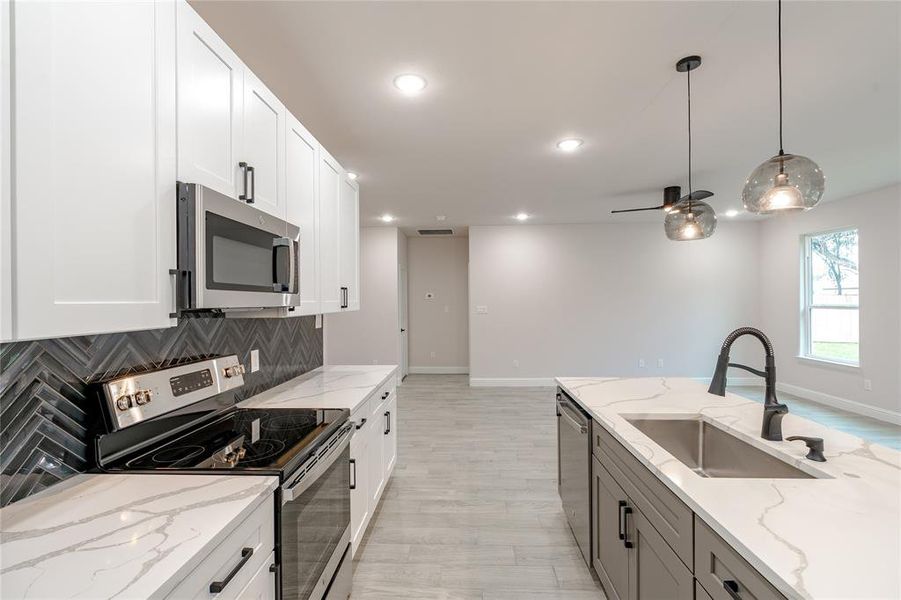 Kitchen with pendant lighting, white cabinets, sink, light stone countertops, and appliances with stainless steel finishes