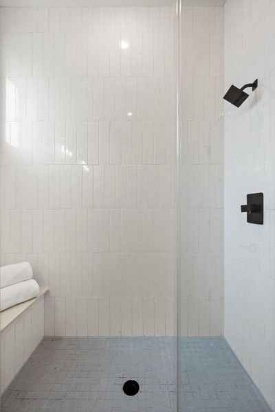 Shower featuring white vertical subway tile walls, a built-in bench, a black square shower head, and a glass partition