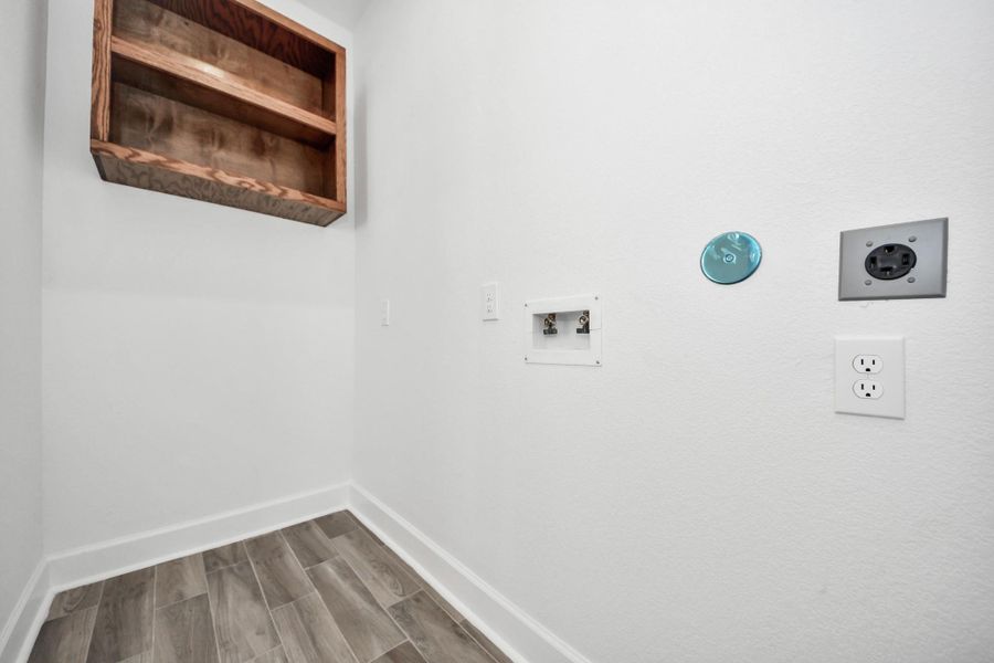 Utility room with connections for a washer and dryer. It features a wall-mounted wooden shelf for storage and has ceramic tile flooring.
