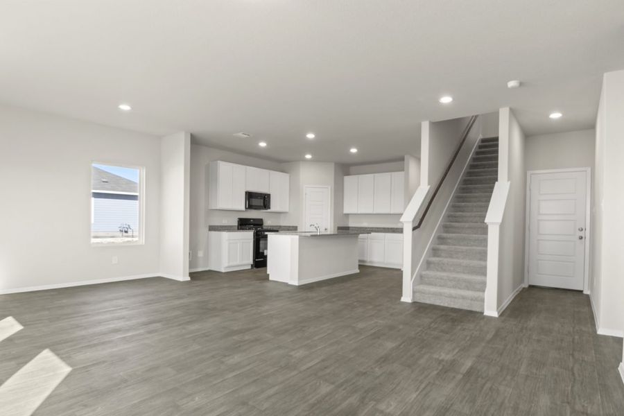 Image of a living room with cream walls, dark brown flooring, an open layout kitchen and a staircase that leads updtairs Image of a living room with cream walls, dark brown flooring, an open layout kitchen and a staircase that leads updtairs