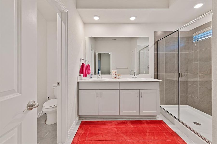 Bathroom with double vanity, a stall shower, a sink, tile patterned flooring, and toilet