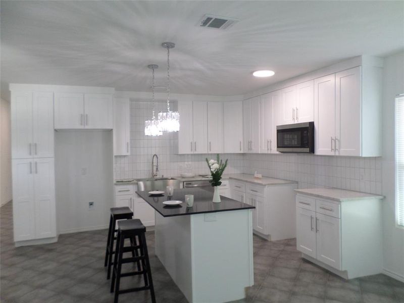 Spacious kitchen featuring an island with a black countertop, white shaker-style cabinetry, subway tile backsplash, and stainless steel microwave