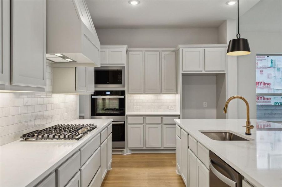 Kitchen featuring stainless steel appliances, light countertops, hanging light fixtures, custom exhaust hood, and tasteful backsplash