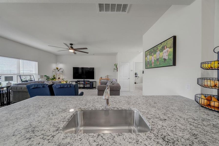 Kitchen featuring light stone countertops, ceiling fan, open floor plan, and carpet