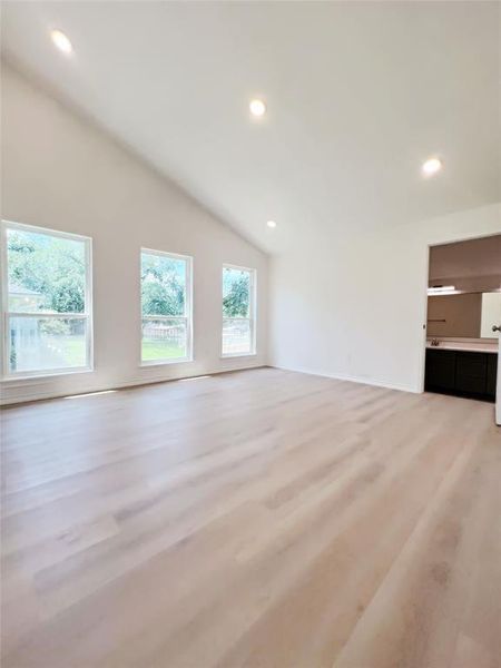 Vaulted ceiling featuring recessed lighting, three large windows, light wood-finish flooring, and a partial view of built-in cabinetry with a countertop