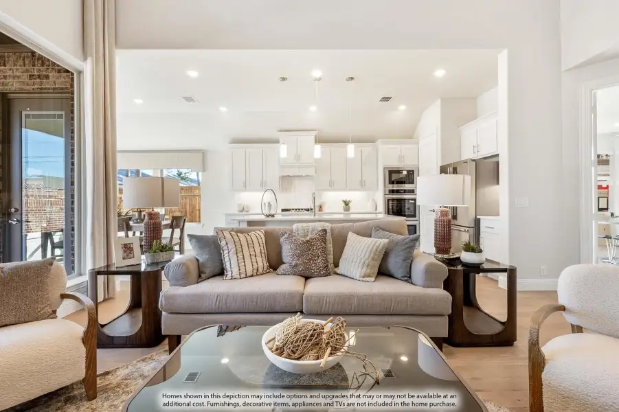 Open-concept living room with gray sofa and glass coffee table, open to kitchen with white cabinets and stainless appliances