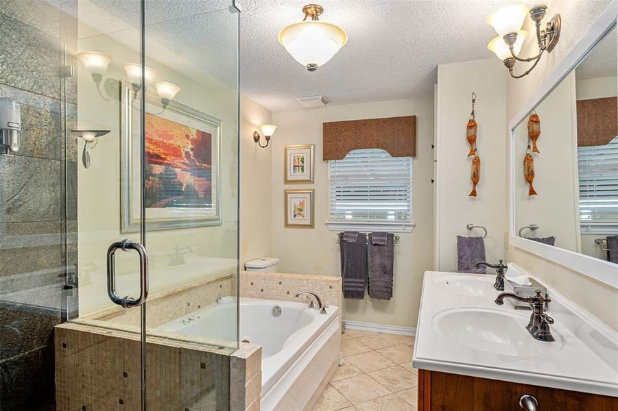 Bathroom featuring a glass-enclosed shower, a built-in tub with tile surround, a window with blinds, a vanity with dual sinks, and ceramic tile flooring