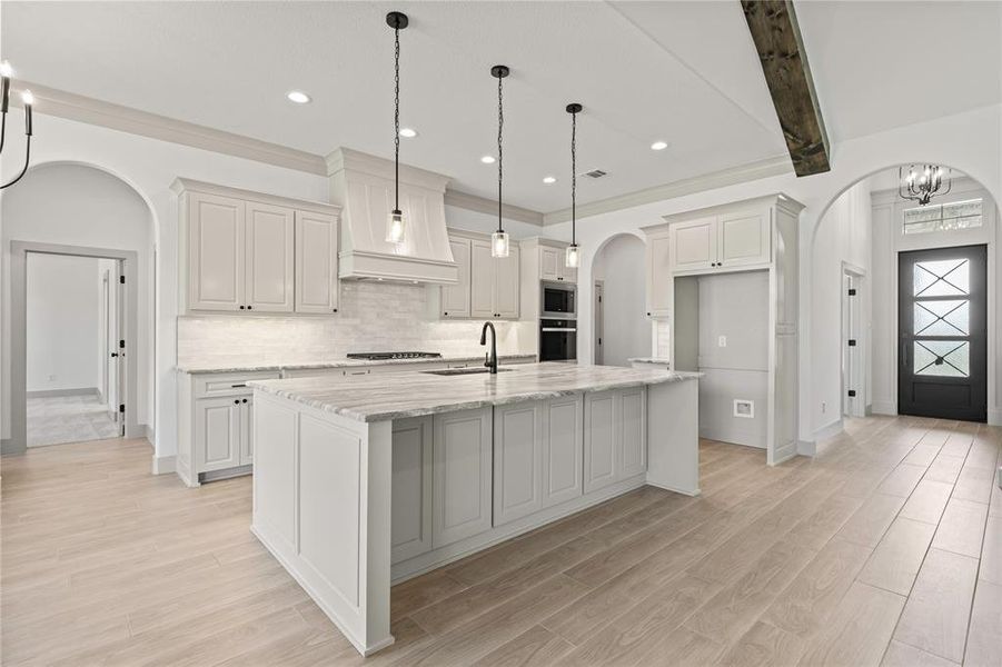 Kitchen with arched walkways, appliances with stainless steel finishes, a kitchen island with sink, tasteful backsplash, and light wood-type flooring Kitchen with arched walkways, appliances with stainless steel finishes, a kitchen island with sink, tasteful backsplash, and light wood-type flooring