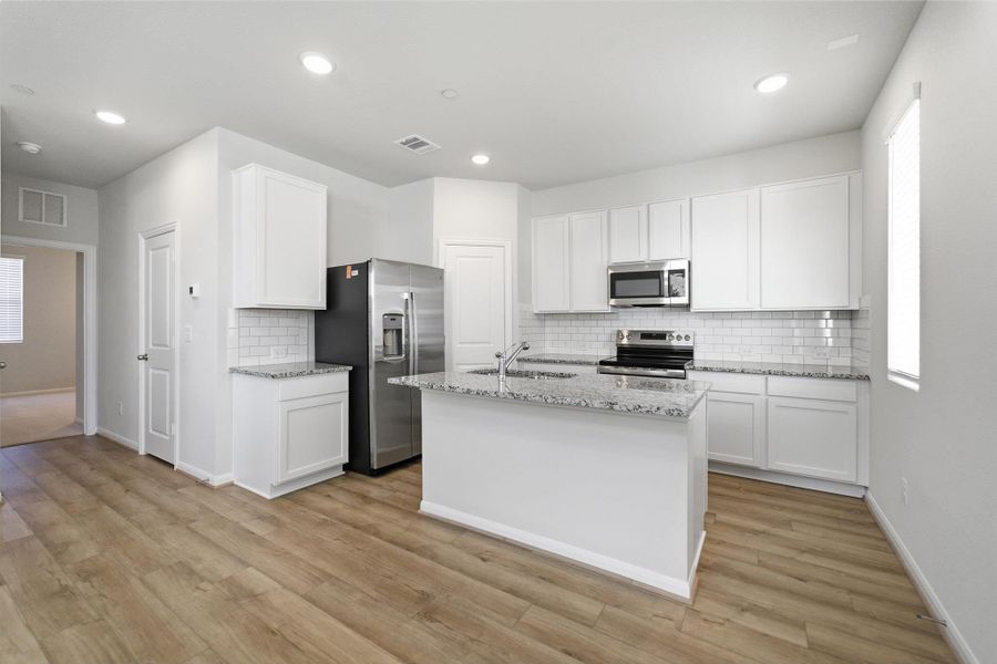 Kitchen featuring white cabinets, light stone countertops, stainless steel appliances, decorative backsplash, and an island with sink