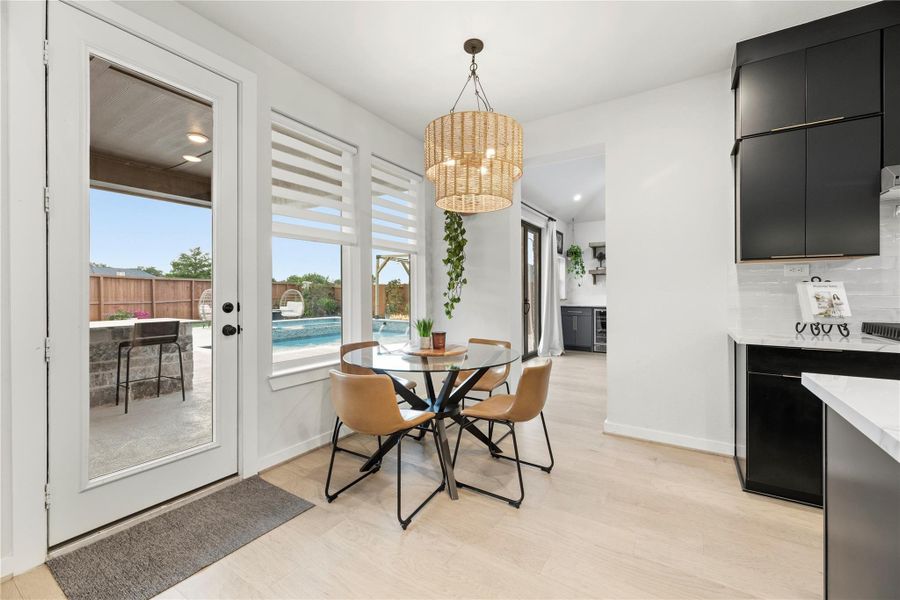 This bright breakfast area features a woven pendant light and views of the pool through large windows and a glass door. The space flows into the kitchen with sleek black cabinetry, creating a seamless open-concept layout. It also gives access to the extra room that was an extension to the property.