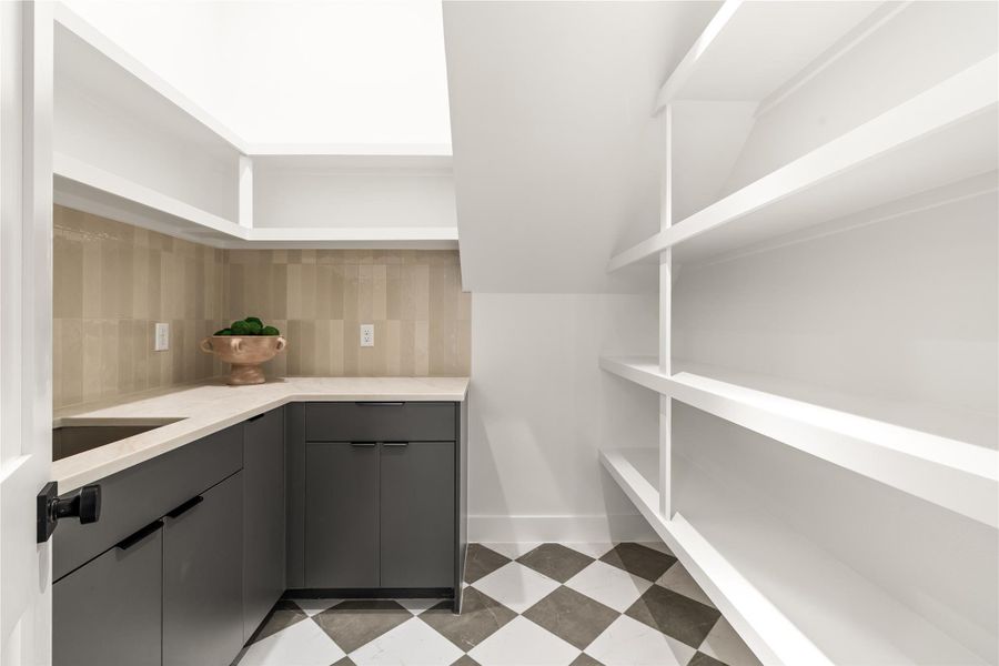 Tucked under the stairs is a full-sized butler pantry, complete with a separate sink and counter area for prep or storing countertop appliances (coffee maker / espresso machine, toaster over, mixer, etc) out of site. Shelving and cabinets offer even more storage space. Tucked under the stairs is a full-sized butler pantry, complete with a separate sink and counter area for prep or storing countertop appliances (coffee maker / espresso machine, toaster over, mixer, etc) out of site. Shelving and cabinets offer even more storage space.
