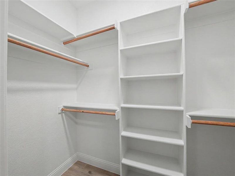 Built-in closet system featuring multiple shelves, three hanging rods, white cabinetry, and wood-finish flooring