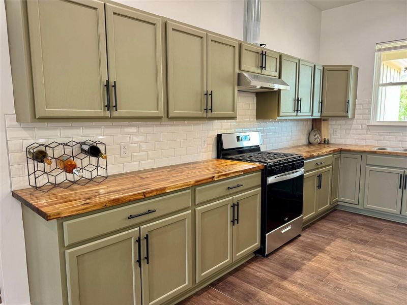 Kitchen featuring gas range, wooden counters, backsplash, dark wood-style floors, and under cabinet range hood Kitchen featuring gas range, wooden counters, backsplash, dark wood-style floors, and under cabinet range hood