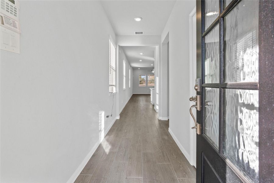 This entryway features a modern, open-concept design. The long, bright corridor utilizes a neutral color palette, recessed lighting, and Luxury Vinyl plank flooring to lead the eye toward the home's main living area.