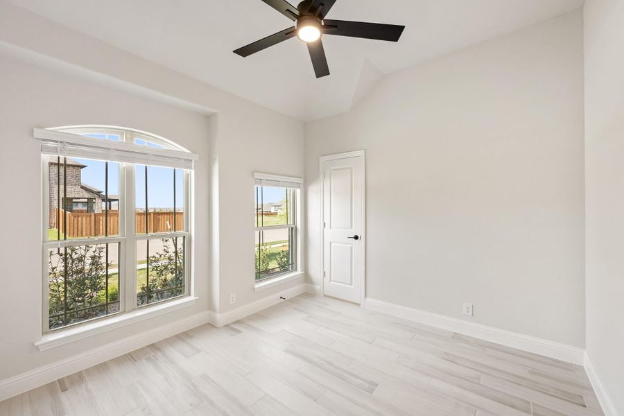 Empty bedroom with light wood floors, ceiling fan, and arched windows overlooking backyard Empty bedroom with light wood floors, ceiling fan, and arched windows overlooking backyard