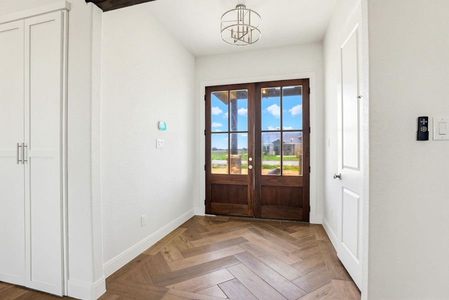 Herringbone wood-look flooring creates a distinguished entry, guiding guests to the double front doors.