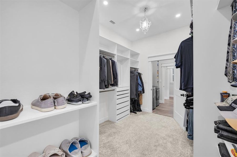 Spacious closet with light colored carpet, washer / dryer, and a chandelier