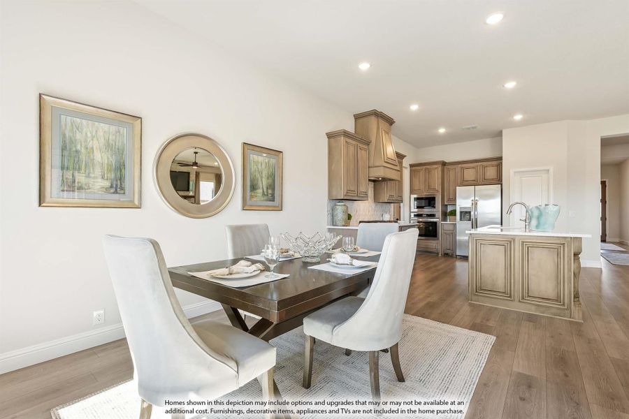 Open dining area with dark wood table and white chairs, flowing into kitchen with stainless appliances and island Open dining area with dark wood table and white chairs, flowing into kitchen with stainless appliances and island