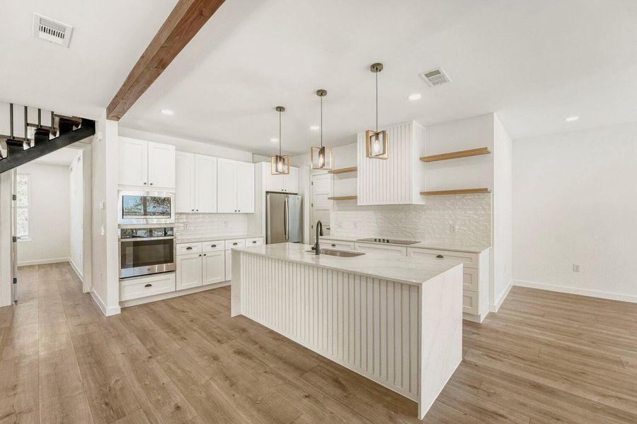 Kitchen featuring a kitchen island with sink, open shelves, light stone counters, stainless steel appliances, and decorative light fixtures