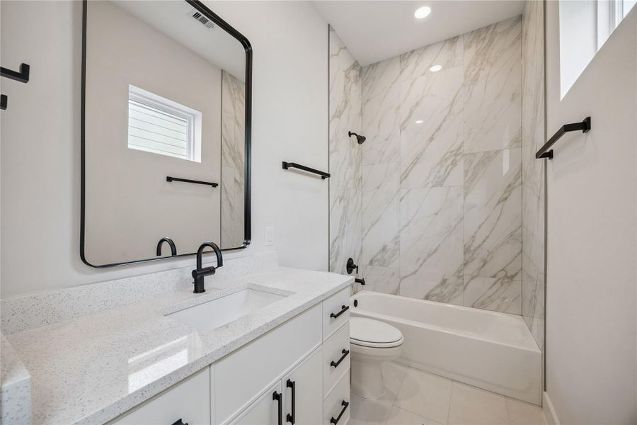 The bath features quartz countertops, modern fixtures, and a glass-enclosed tub and shower combination with full-height tile surround. Clean contemporary fixtures and a bright neutral palette keep the space cohesive with the rest of the home’s design. (digitally staged) The bath features quartz countertops, modern fixtures, and a glass-enclosed tub and shower combination with full-height tile surround. Clean contemporary fixtures and a bright neutral palette keep the space cohesive with the rest of the home’s design. (digitally staged)