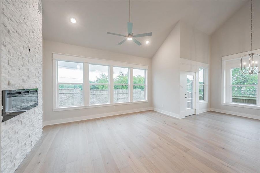 Unfurnished living room featuring light wood finished floors, high vaulted ceiling, a ceiling fan, a chandelier, and recessed lighting