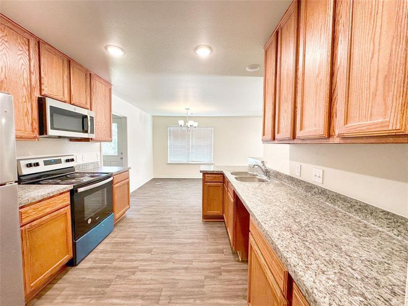 Kitchen featuring hanging light fixtures, sink, stainless steel appliances, a notable chandelier, and light hardwood / wood-style floors