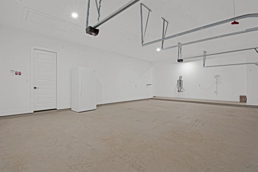 True 3-Car Garage featuring a 5ft bump out and side access door to yard, freestanding upright freezer, tankless water heater (gas), plumbed for water-softener, recessed lighting, and 2 garage doors