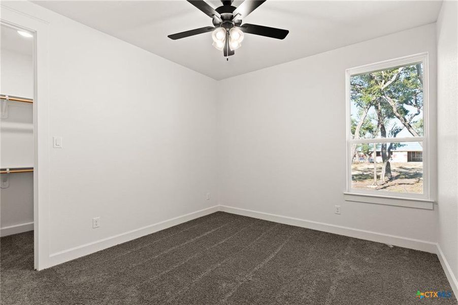 Unfurnished bedroom featuring a spacious closet, dark colored carpet, and a ceiling fan