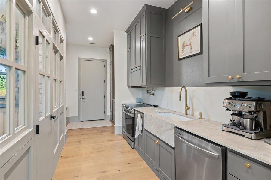 Kitchen featuring light hardwood / wood-style flooring, stainless steel appliances, gray cabinets, light stone counters, and sink