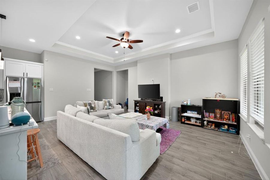 Living room featuring ceiling fan, light wood-style floors, recessed lighting, a tray ceiling, and crown molding