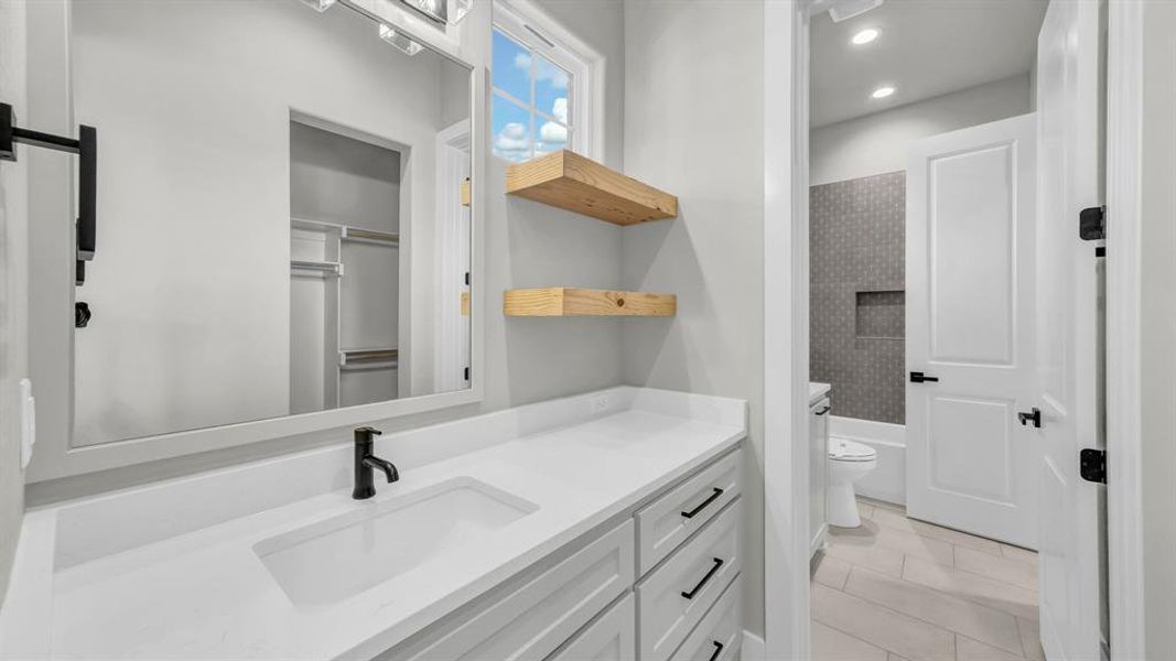 Bathroom featuring a white vanity with an integrated sink and matte black faucet, a large framed mirror, and two floating wood shelves