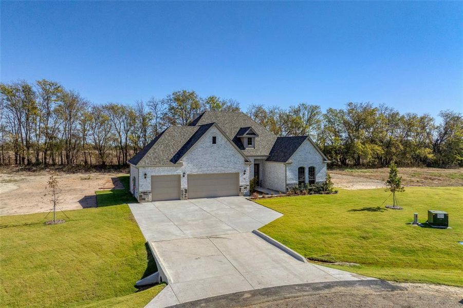 French country inspired facade featuring stone siding, driveway, a front lawn, an attached garage, and a shingled roof French country inspired facade featuring stone siding, driveway, a front lawn, an attached garage, and a shingled roof