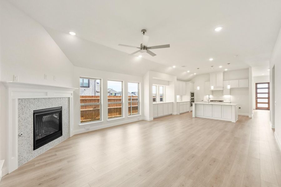 Open-concept living room with fireplace, vaulted ceiling, and light wood floors flowing into white kitchen