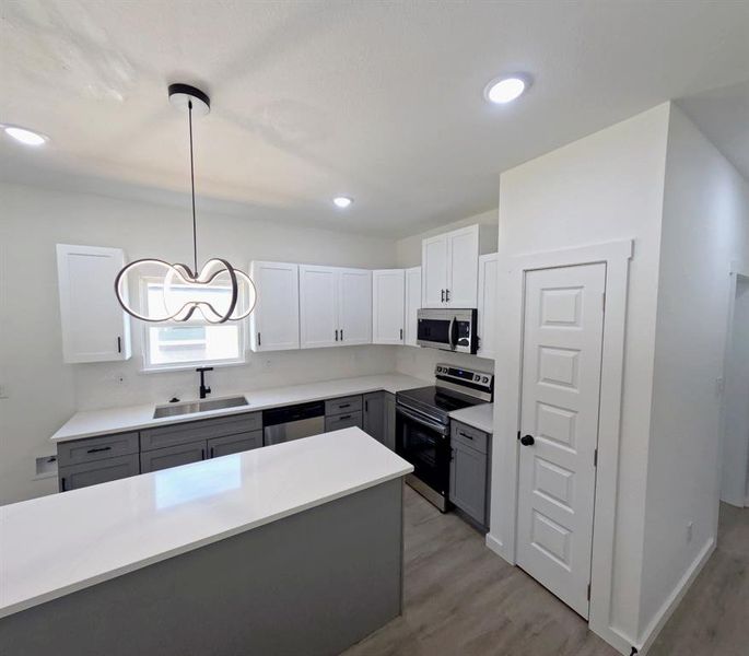 Kitchen with gray cabinets, appliances with stainless steel finishes, white cabinets, decorative light fixtures, and light wood-style floors Kitchen with gray cabinets, appliances with stainless steel finishes, white cabinets, decorative light fixtures, and light wood-style floors