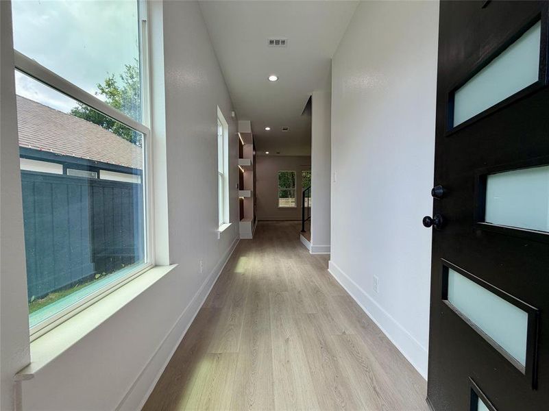 Entryway featuring a contemporary black door with frosted glass inserts, wood-finish flooring, recessed lighting, built-in shelving, and white baseboards Entryway featuring a contemporary black door with frosted glass inserts, wood-finish flooring, recessed lighting, built-in shelving, and white baseboards