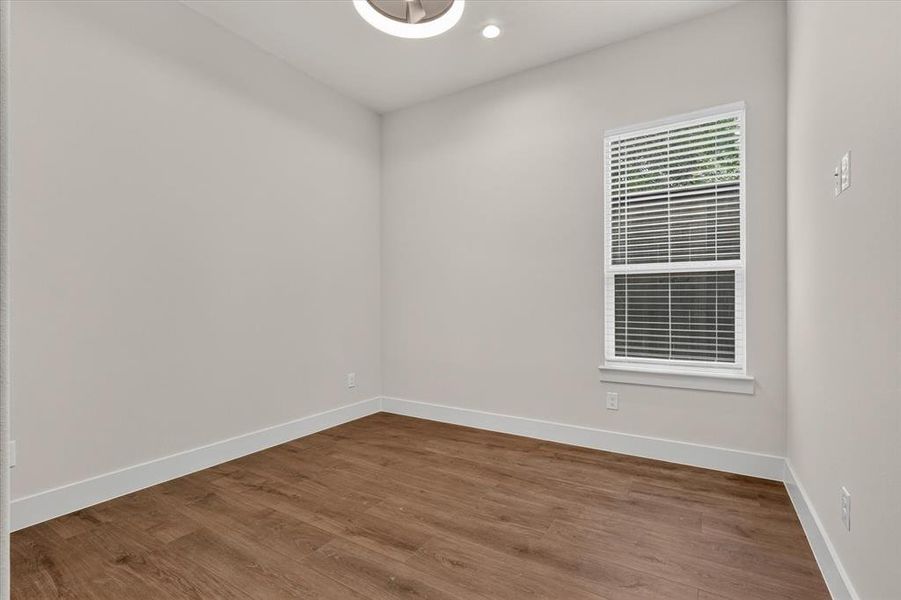 Neutral wall color with wood-finish flooring, white baseboards, and a single window with blinds