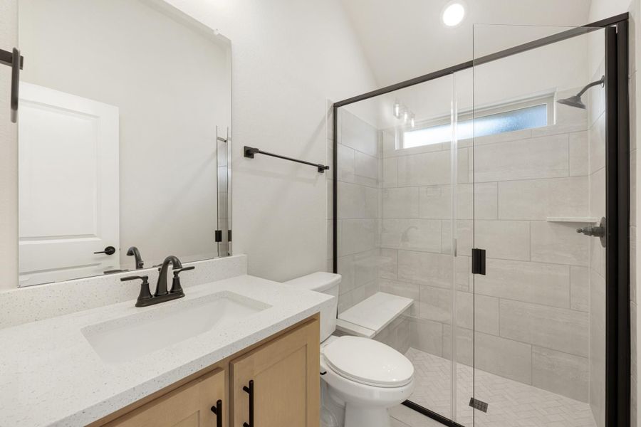 Bathroom with quartz vanity, wood cabinets, glass walk-in shower with tile walls, and black hardware fixtures