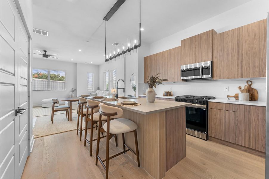 The kitchen, the heart of the second-floor open-concept living, dining, and kitchen, features a spacious island with a one-sided cascade quartz countertop, farmhouse sink, and modern pendant lights, complemented by an abundance of sleek, modern cabinetry providing ample storage, perfect for meal prep, casual breakfasts, or gathering with family and friends.