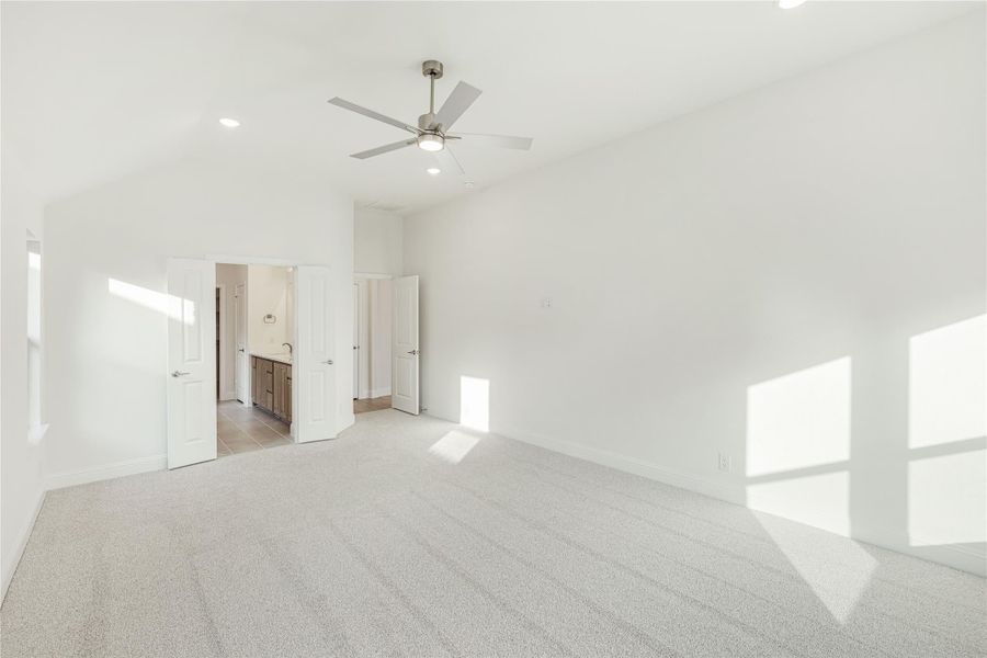 Empty master bedroom with carpet, ceiling fan, and open doors to ensuite bathroom and closet