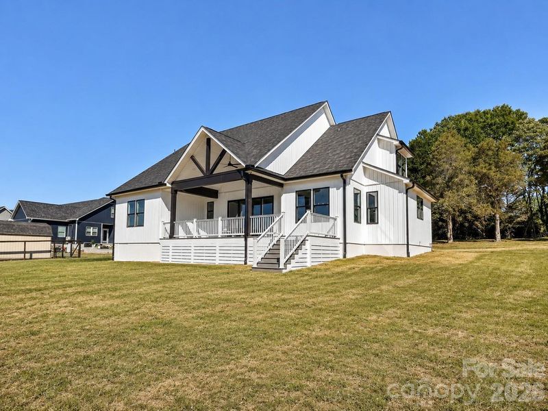Rear elevation showcases charming modern farmhouse architecture, a covered back deck, and a spacious backyard backing to mature trees for added privacy. (Concept grass)