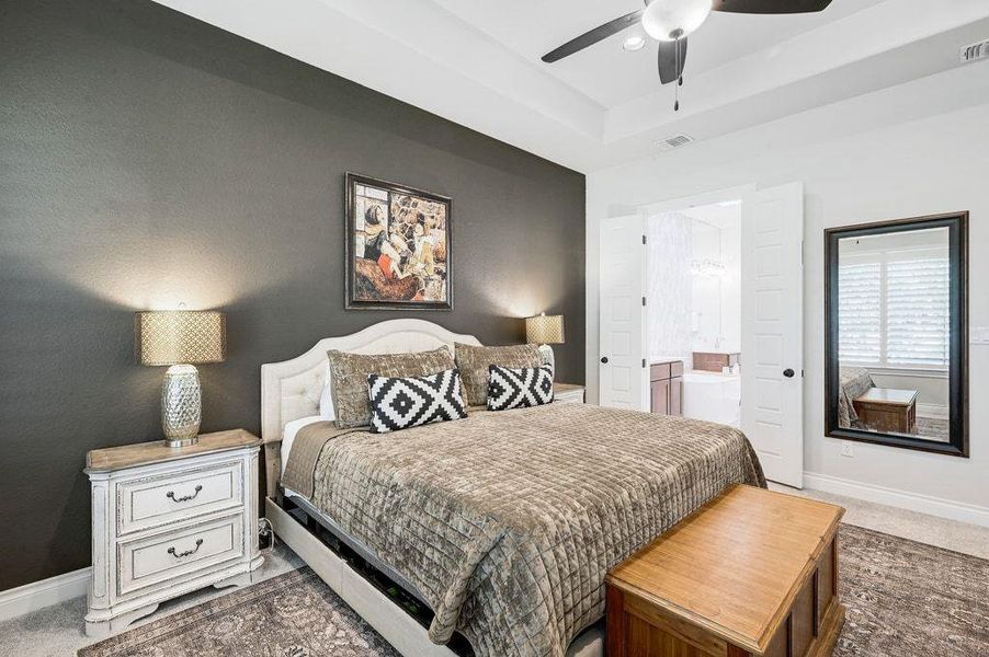 Bedroom featuring carpet, a ceiling fan, connected bathroom, and a raised ceiling Bedroom featuring carpet, a ceiling fan, connected bathroom, and a raised ceiling