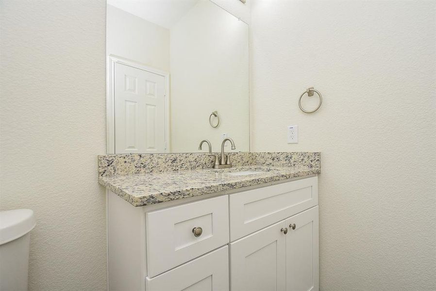 A clean, white bathroom with a granite countertop, white cabinets, a mirror, and modern fixtures.