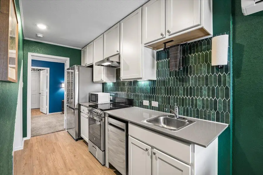 Kitchen featuring a textured wall, backsplash, white cabinetry, stainless steel appliances, and light wood-style flooring Kitchen featuring a textured wall, backsplash, white cabinetry, stainless steel appliances, and light wood-style flooring