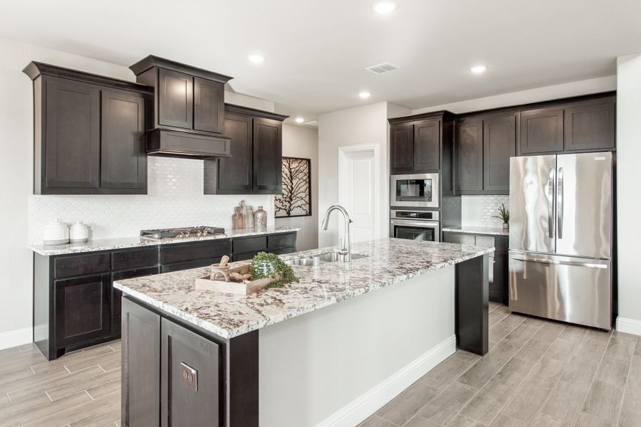 Kitchen with dark cabinets, granite island, stainless steel appliances, and wood-look tile floors Kitchen with dark cabinets, granite island, stainless steel appliances, and wood-look tile floors