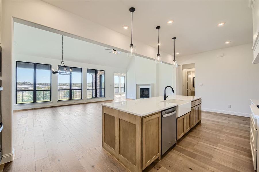 Kitchen featuring light wood-type flooring, a kitchen island with sink, stainless steel dishwasher, ceiling fan with notable chandelier, and hanging light fixtures