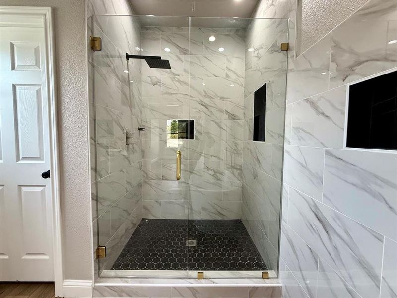 Bathroom featuring a marble finish shower, a textured wall, and wood finished floors
