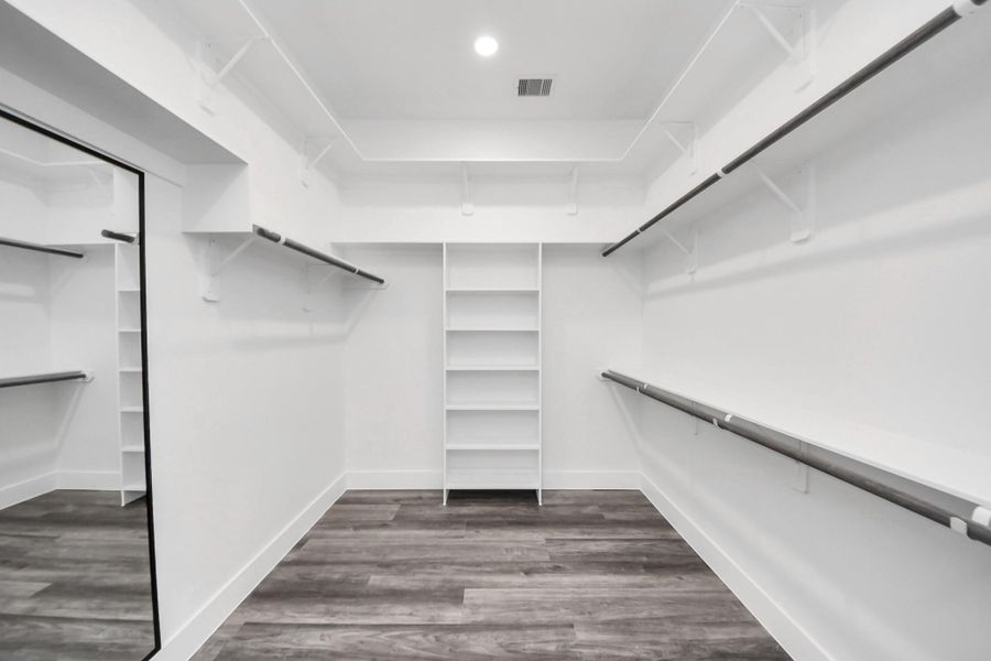 This photo shows a spacious walk-in closet with ample shelving and hanging space, featuring modern, light-colored walls and flooring, and a full-length mirror. This photo shows a spacious walk-in closet with ample shelving and hanging space, featuring modern, light-colored walls and flooring, and a full-length mirror.