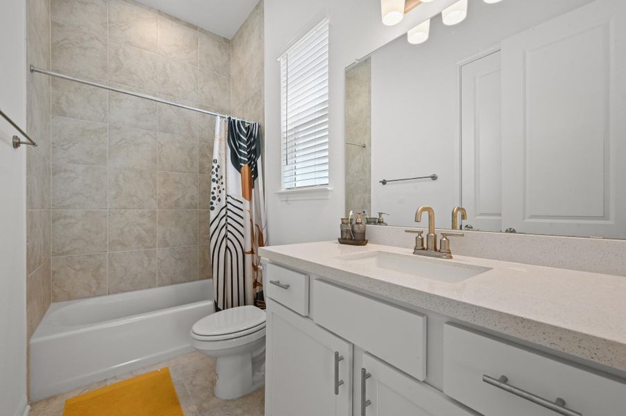 Tiled walls surround the shower and tub adjacent to a vanity with stone counters.